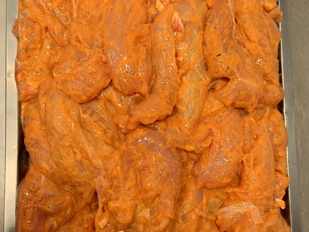 Photo réelle : tenders de poulet marinés, crus, dans un bac inox.