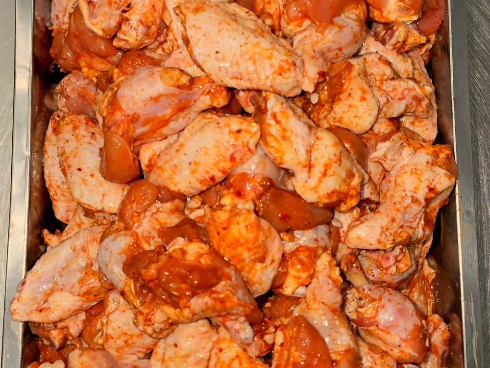 Photo réelle : wings de poulet marinées, crues, dans un bac inox.